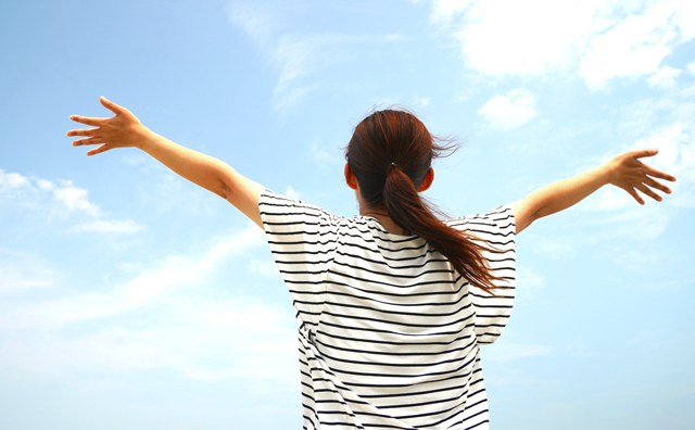 青空に向かって伸びをする女性